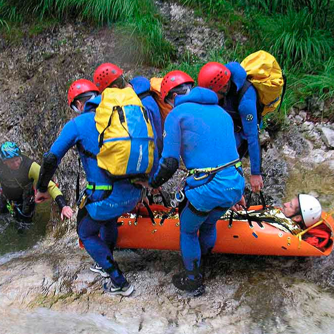 Cuatro rescatistas bajando la camilla Sked con víctima por barranco de agua.