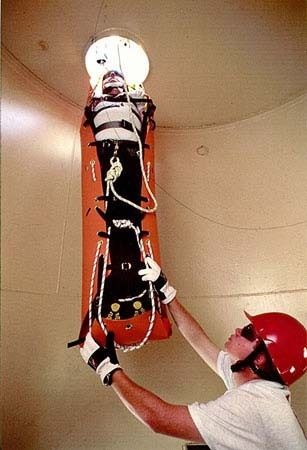 Camilla de rescate en posición vertical saliendo por boca de hombre estrecha.